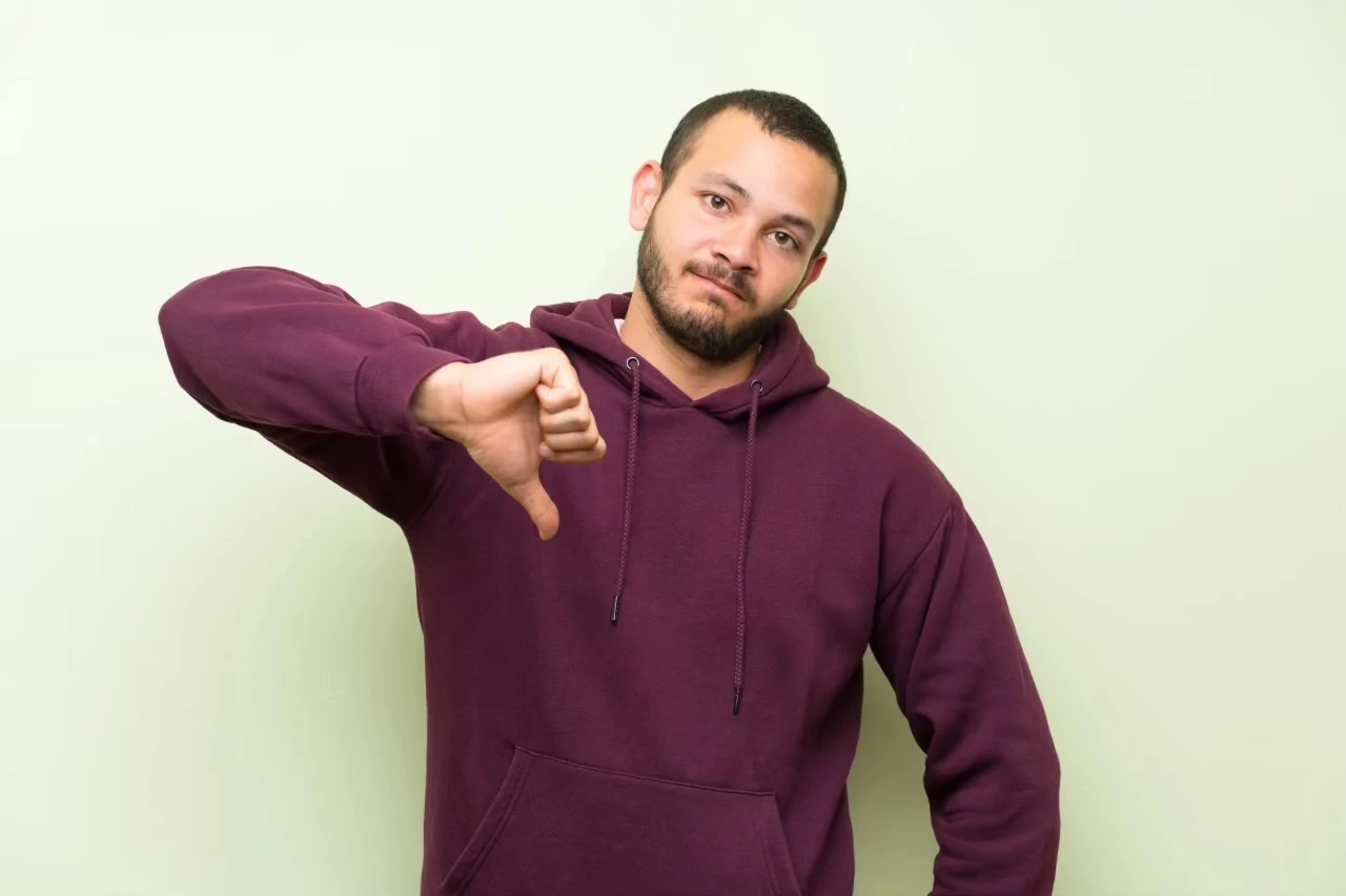 junger Mann hält einen Daumen nach unten und hat einen negativen Gesichtsausdruck