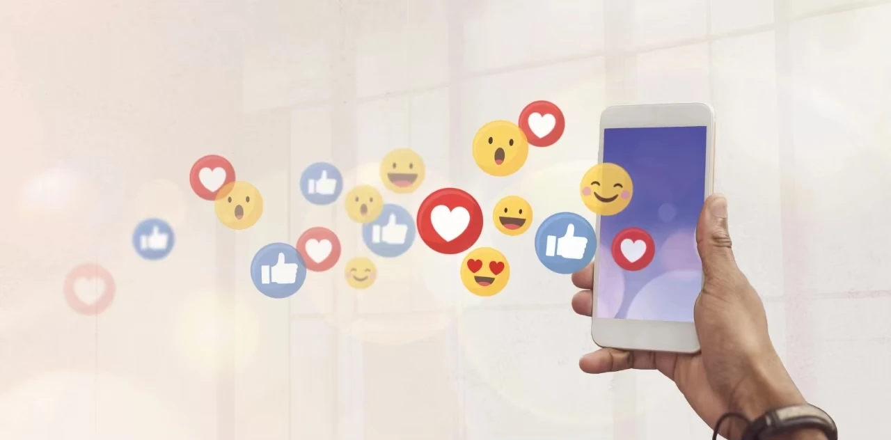 eine Hand hält ein Handy aus dem lauter positive Emoticons fliegen (Herzchen, Smileys, Likes)
