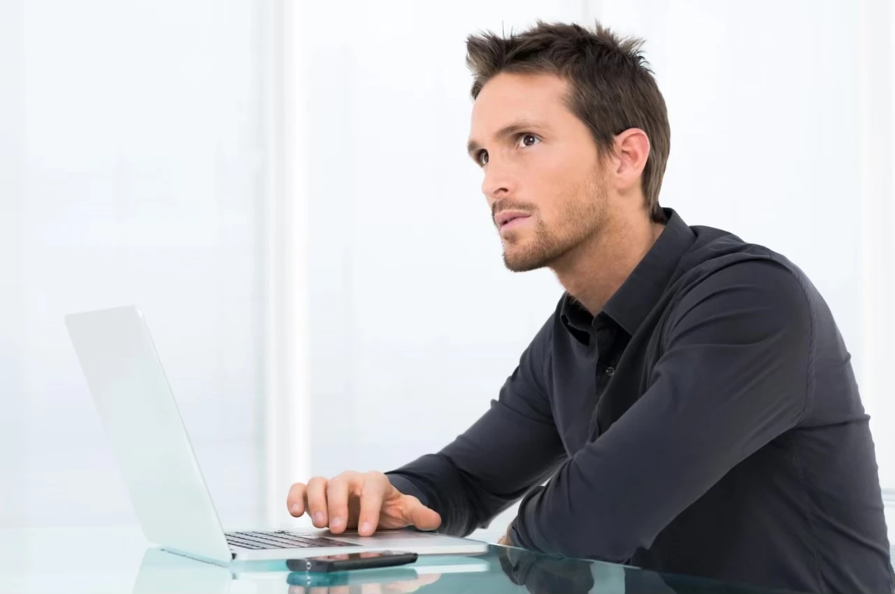 Mann sitzt vor Laptop und schaut fragend