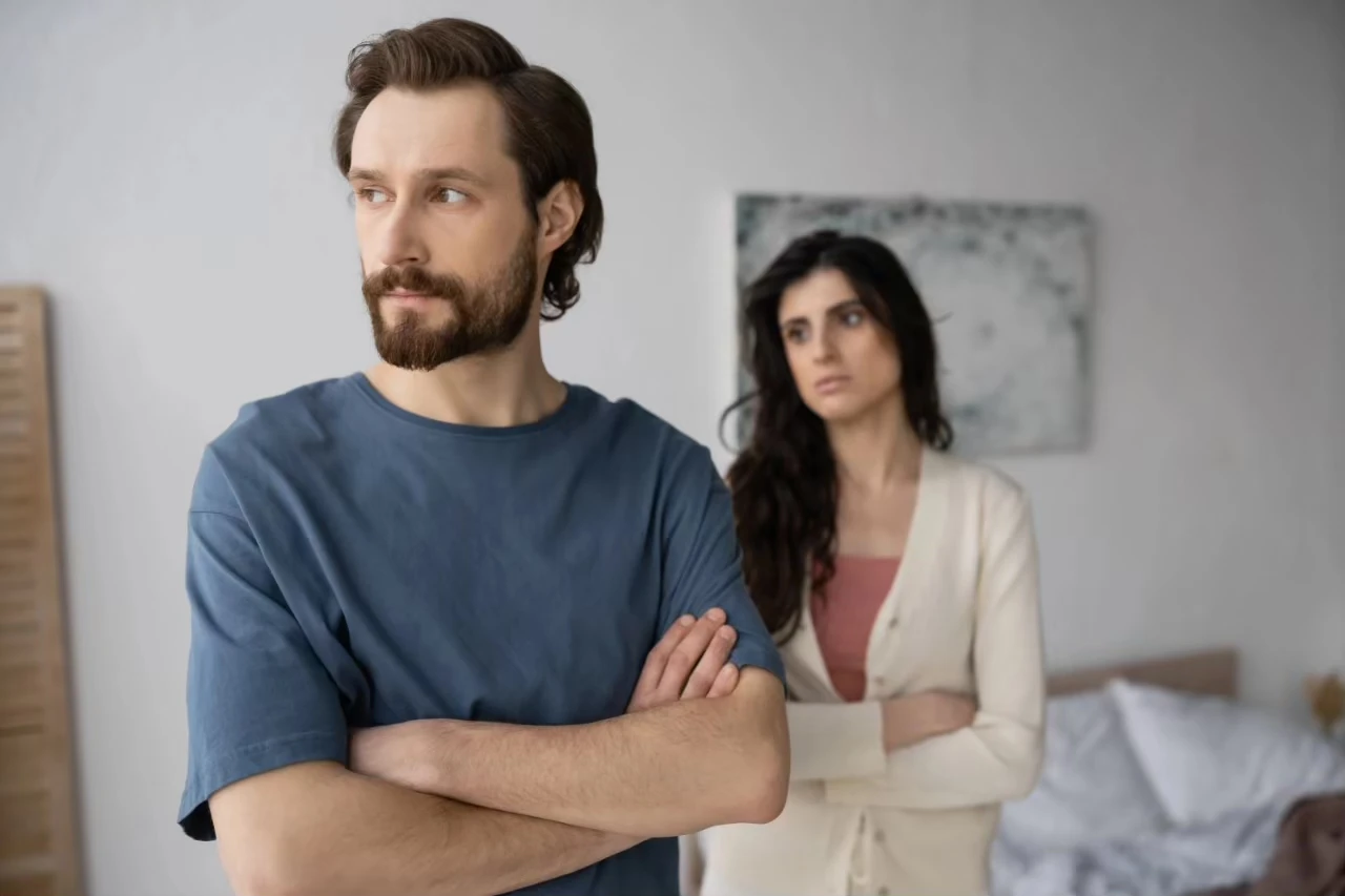 Paar mit verschränkten Armen steht mit Abstand hintereinander, beide gucken links aus dem Bild raus
