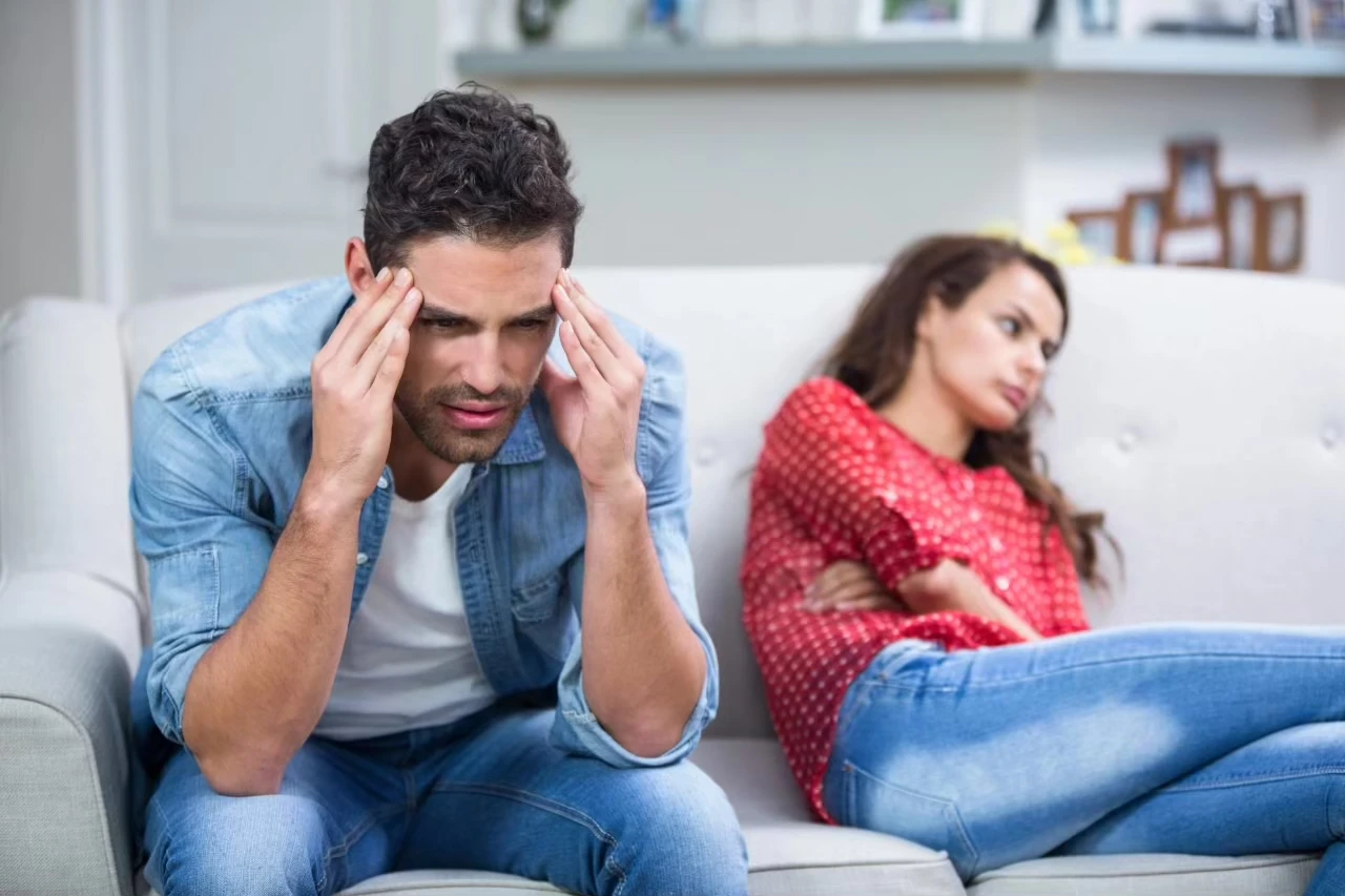 Paar sitzt auf der Couch, Frau hat sich abwehrend weggedreht, Mann hat Hände zum Kopf erhoben