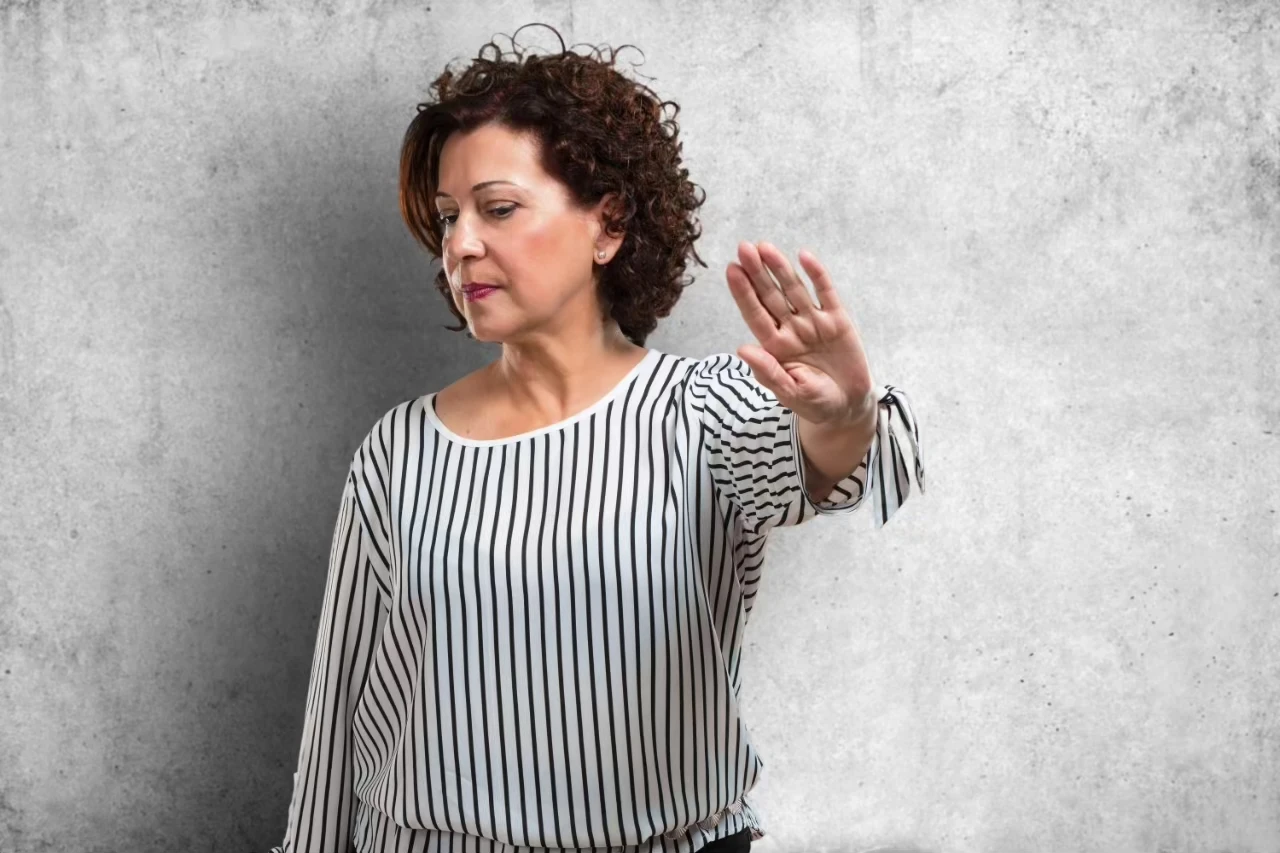 Frau mit gestreiftem Shirt hält eine Hand ablehnend vor sich und dreht sich weg