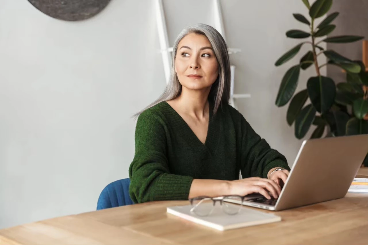 Frau sitzt am Laptop und schaut nachdenklich nach links aus dem Bild raus