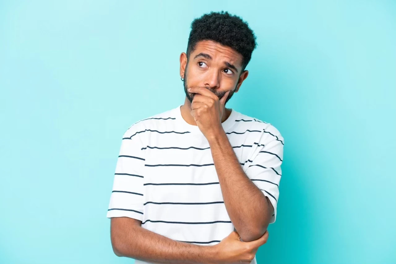 Mann in gestreiftem Shirt hält das Kinn nachdenklich in einer Hand, die andere Hand unterstützt den anderen Arm