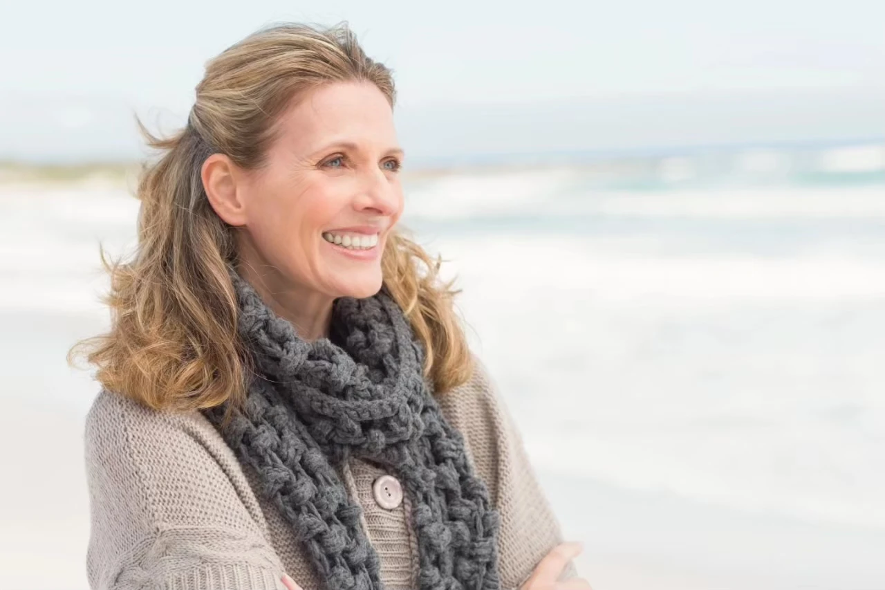 Frau steht am Strand und schaut breit lächelnd aufs Meer