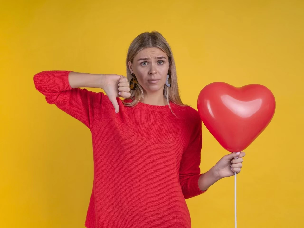 Frau mit Herz-Luftballon in der einen Hand, die andere erhoben mit Daumen, der nach unten zeigt