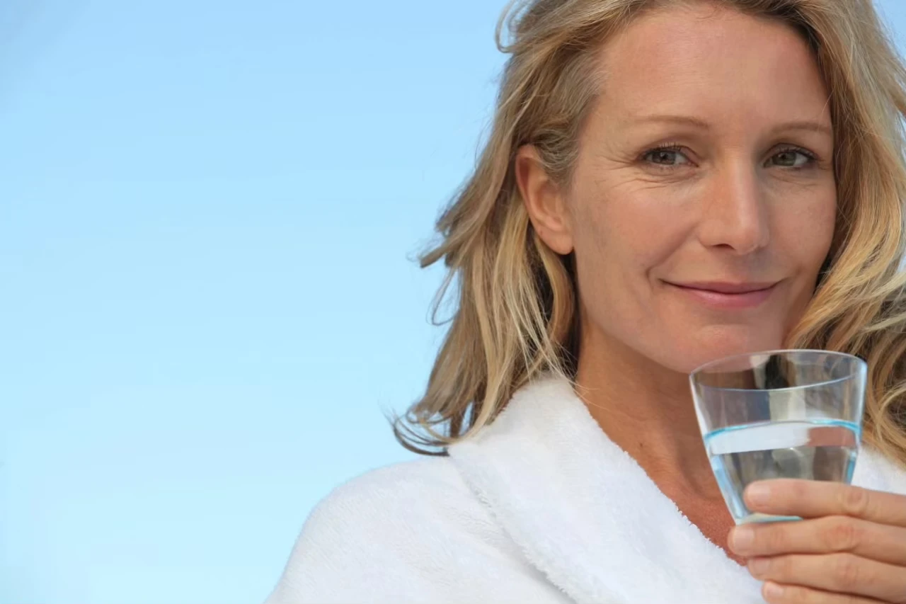 Entspannt lächelnde Frau mit Glas Wasser in der Hand vor blauem Himmel