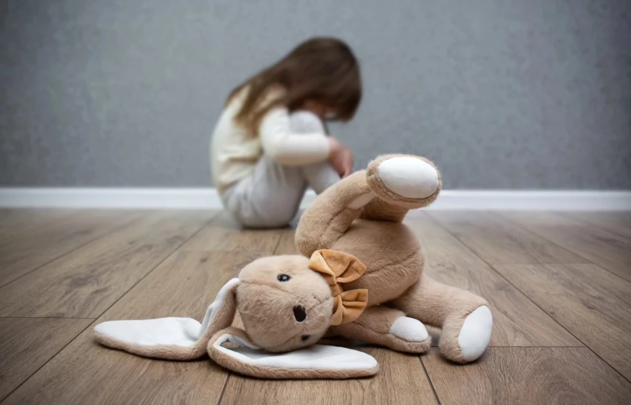 Kleines Kind im Hintergrund zusammengekauert, im Vordergrund ein auf die Seite gefallener Stofftier-Hase