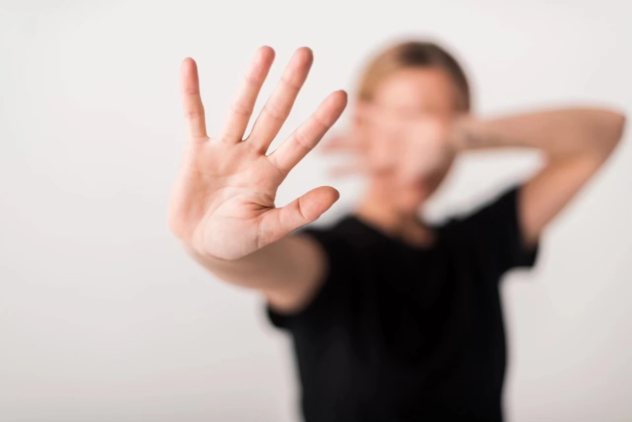 Person hält eine Hand abwehrend vors Gesicht, eine Hand abwehrend in die Kamera