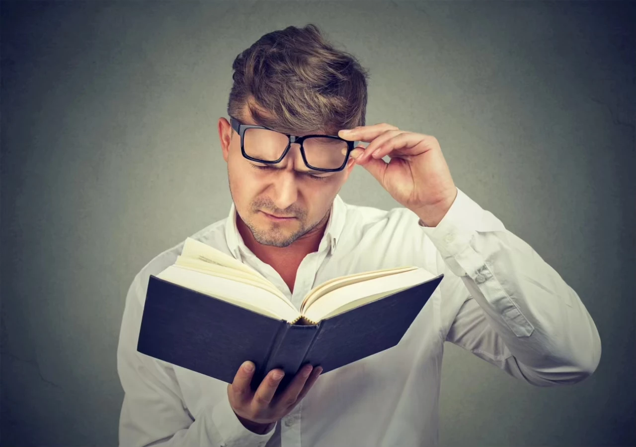 Mann liest stirnrunzelnd und verwundert ein Buch und hebt die Brille auf der Nase hoch
