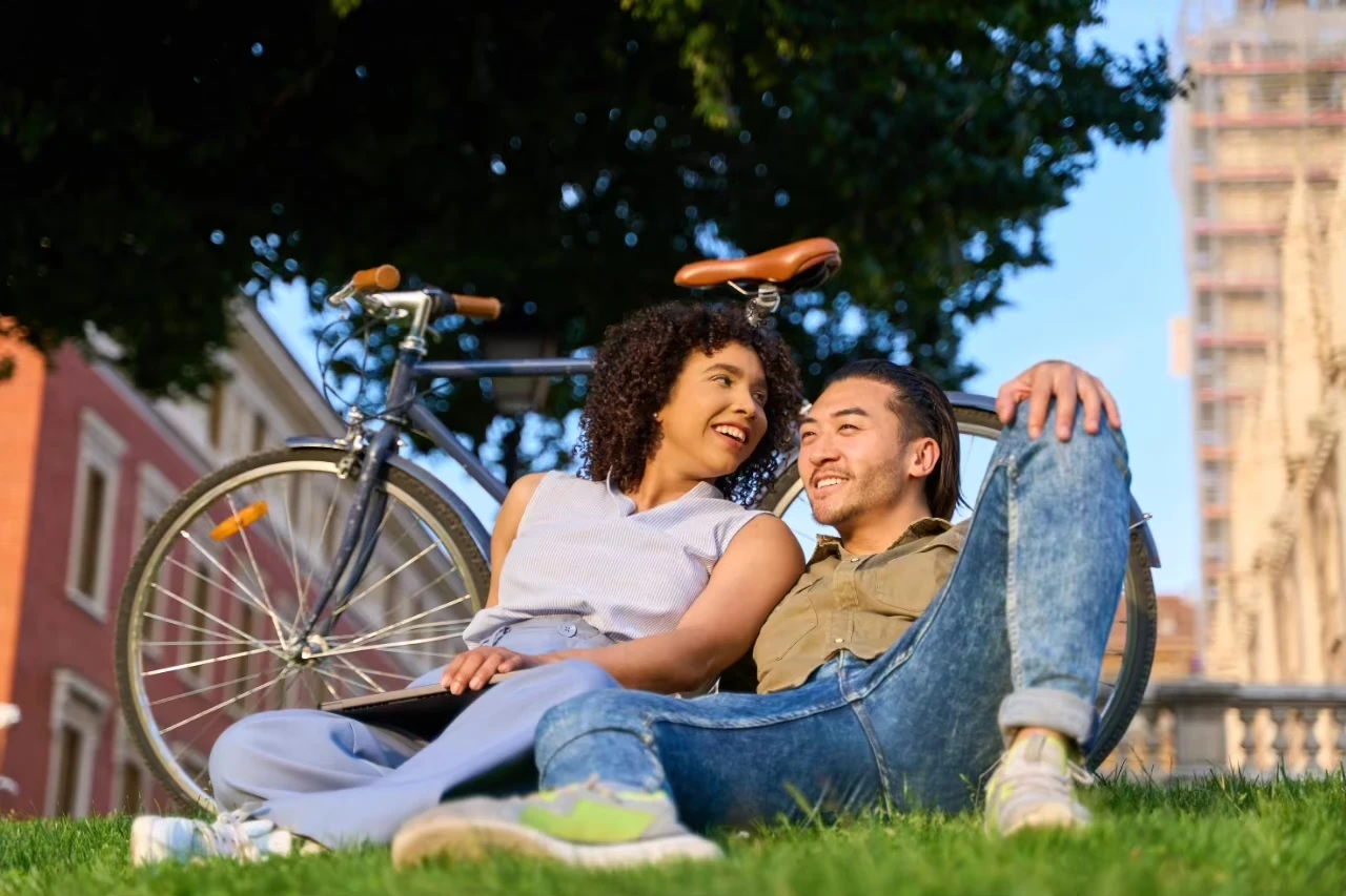 Frau und Mann sitzen lächelnd im Gras vor einem Fahrrad