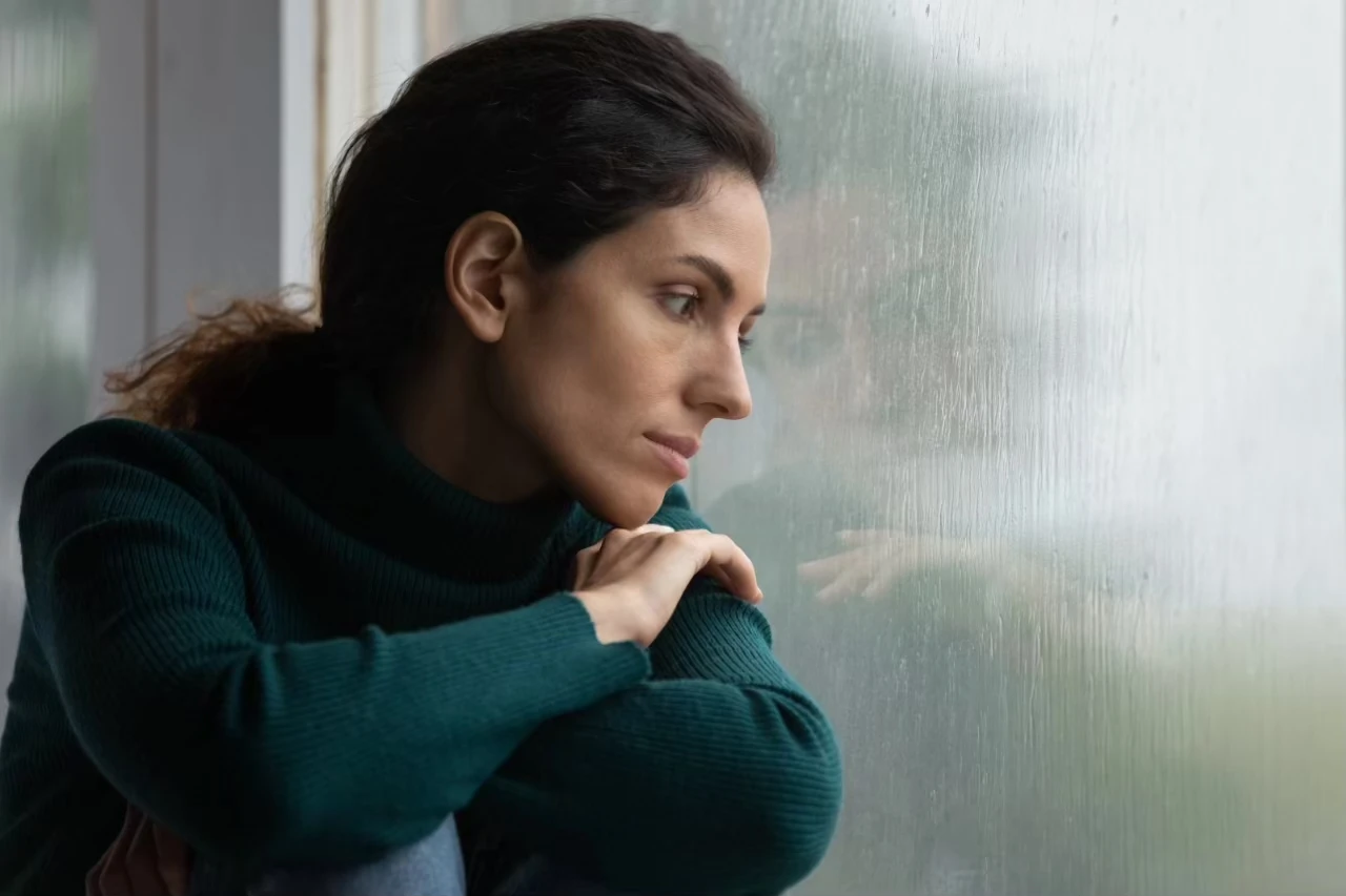 Frau schaut traurig durch ein Fenster, an dem der Regen hinunterläuft