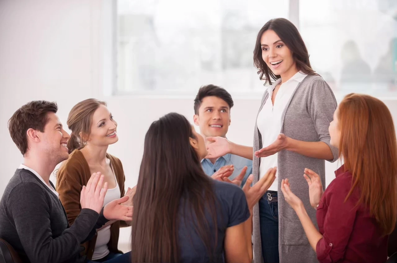 Frau steht sprechend vor einer begeisterten kleinen Runde von Menschen