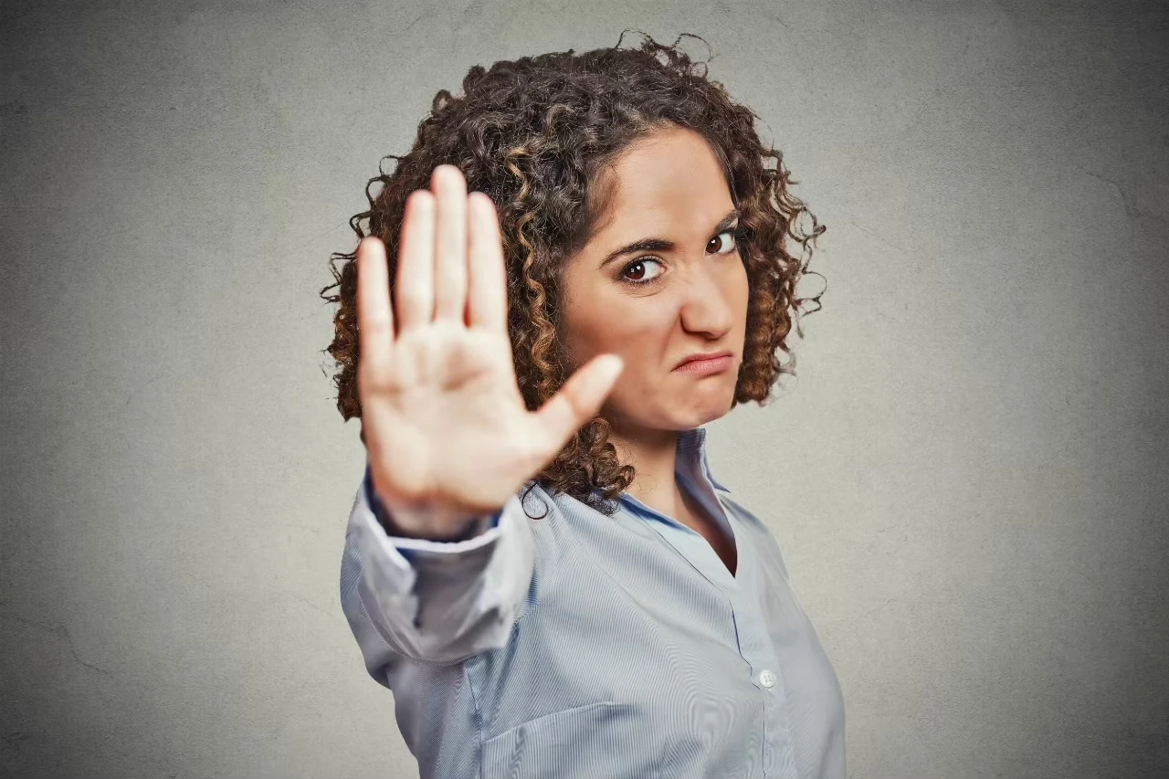 Frau streckt mit angeekeltem Gesichtsausdruck Hand wie ein Stopp-Signal aus
