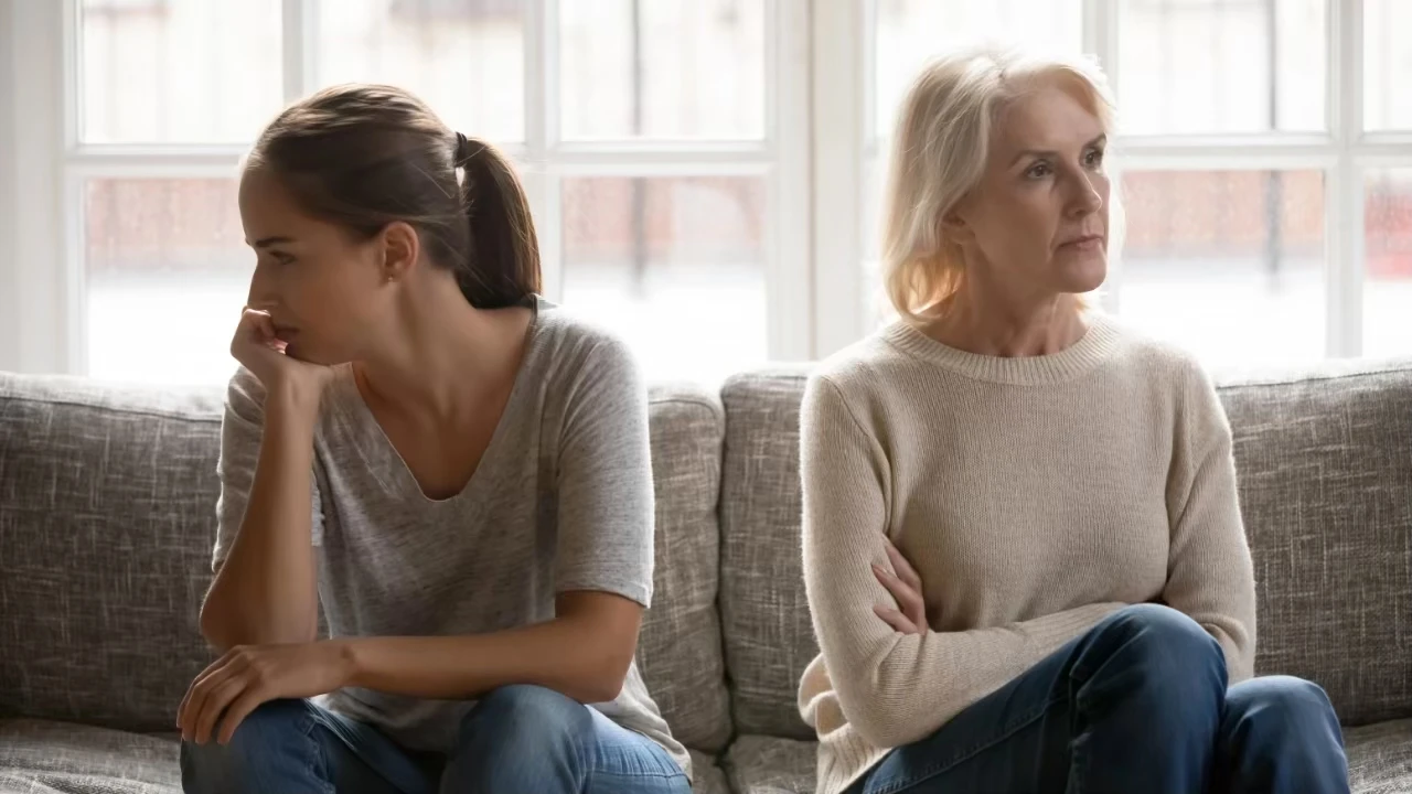 Ältere Frau und jüngere Frau sitzen auf einer Couch, aber voneinander abgewandt
