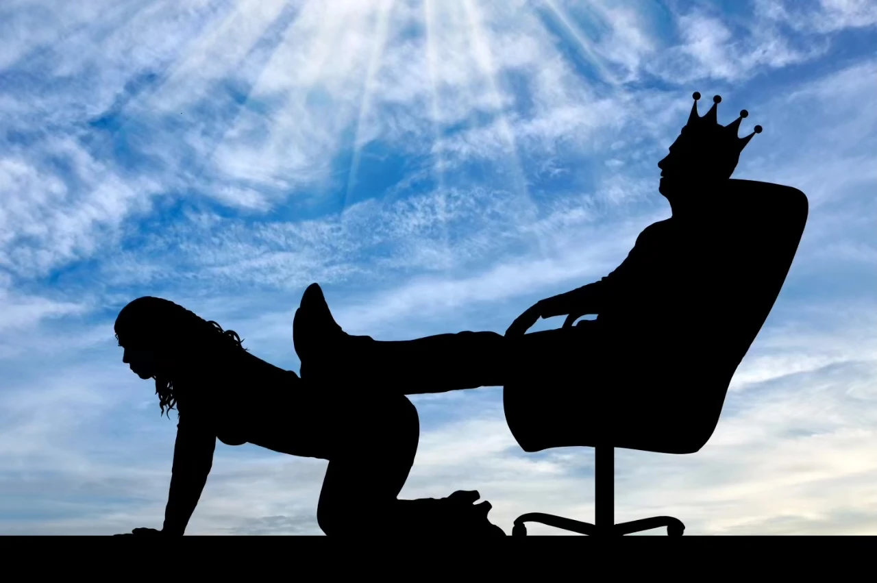Vor blauem, leicht bewölktem Himmel eine Silhouette von einer Person mit Königskrone in einem Chefsessel, die Beine hochgelegt auf eine kniende Person