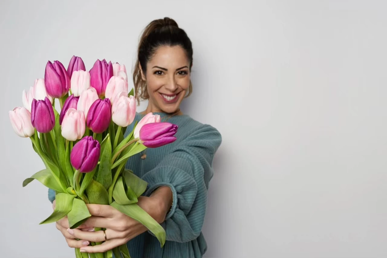 Lächelnde Frau hält Strauß mit rosa- und pinkfarbenen Tulpen in die Kamera