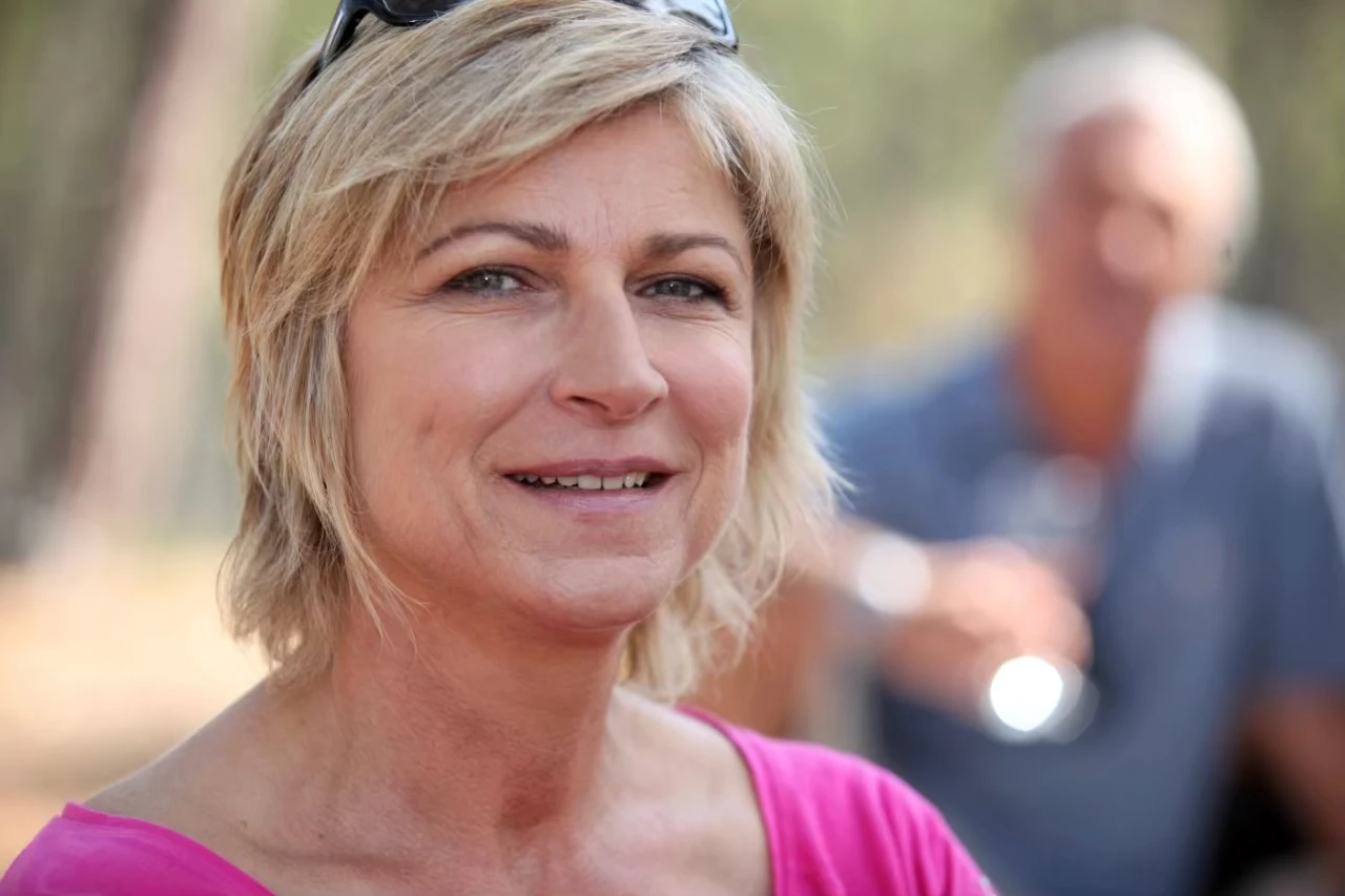 Frau mit blonden kurzen Haaren, Sonnenbrille auf dem Kopf und mit pinkfarbenem Shirt lächelt in die Kamera
