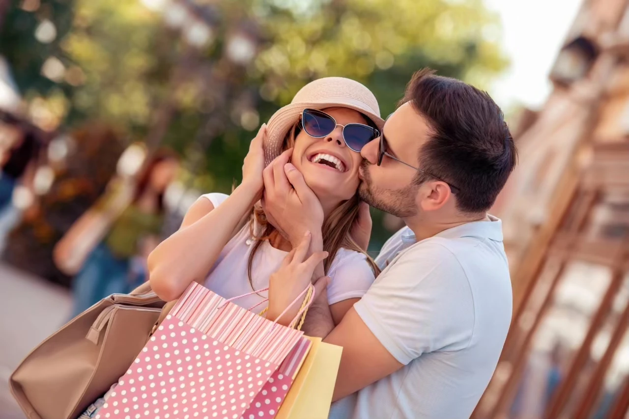 Mann mit Geschenktüten küsst lächelnde Frau auf die Wange