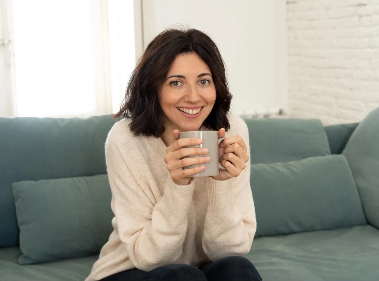 Frau mit Becher in der Hand lächelt entspannt in die Kamera