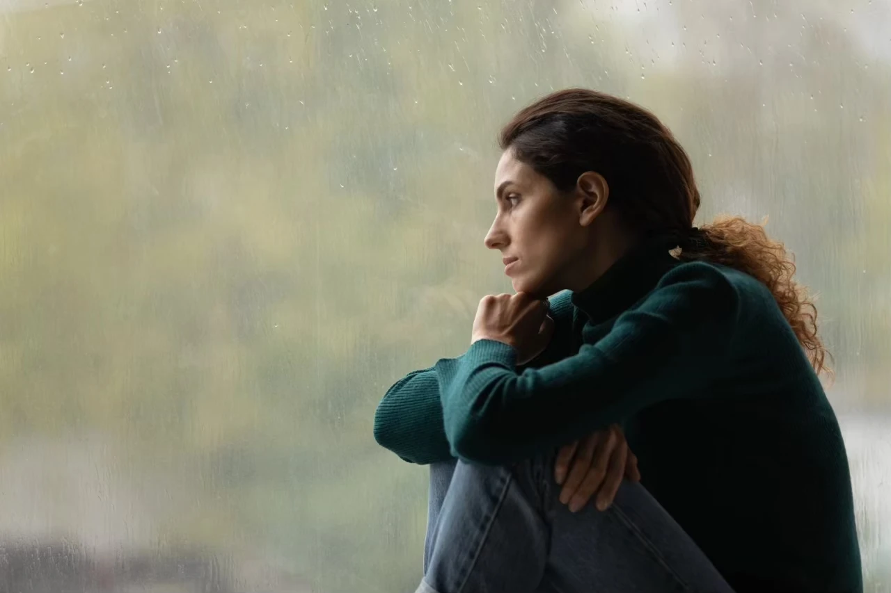 Frau schaut mit traurigem Blick aus dem Fenster
