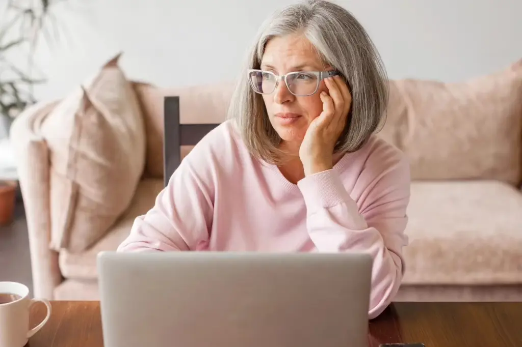 Frau mit verfrüht grauen Haaren sitzt vor einem Laptop